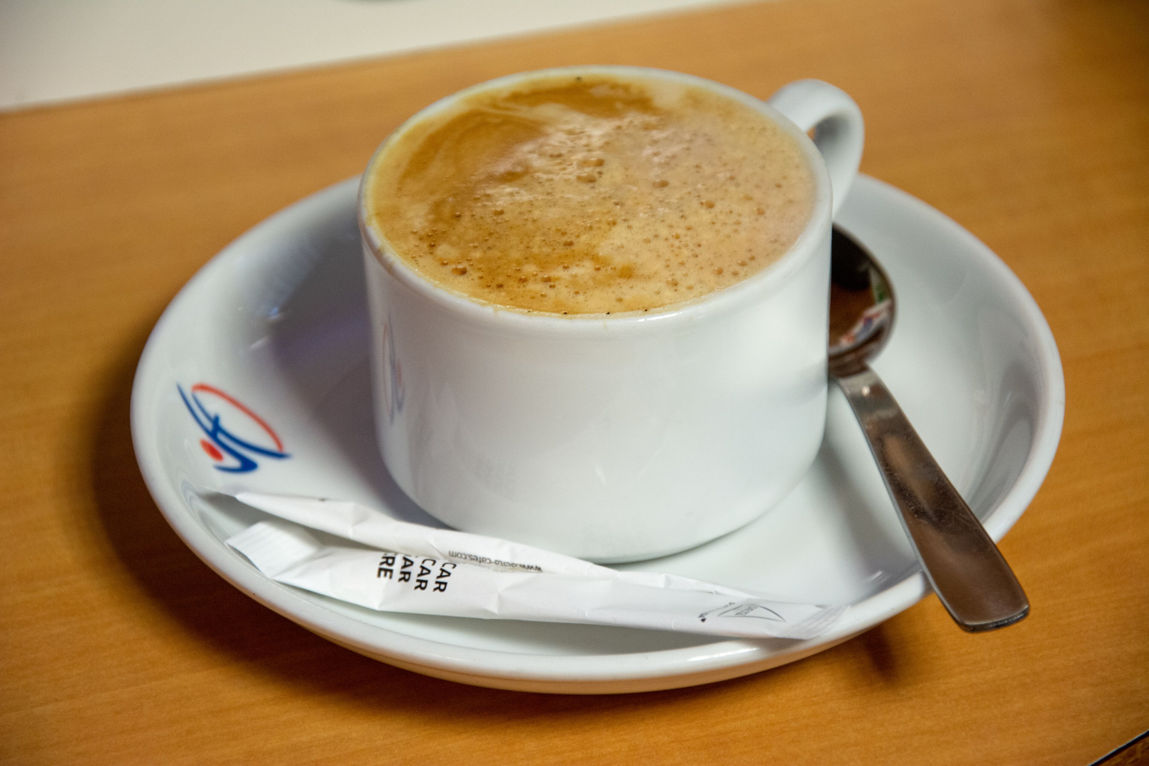 A white cup of coffee with a spoon on a saucer, placed on a wooden table.
