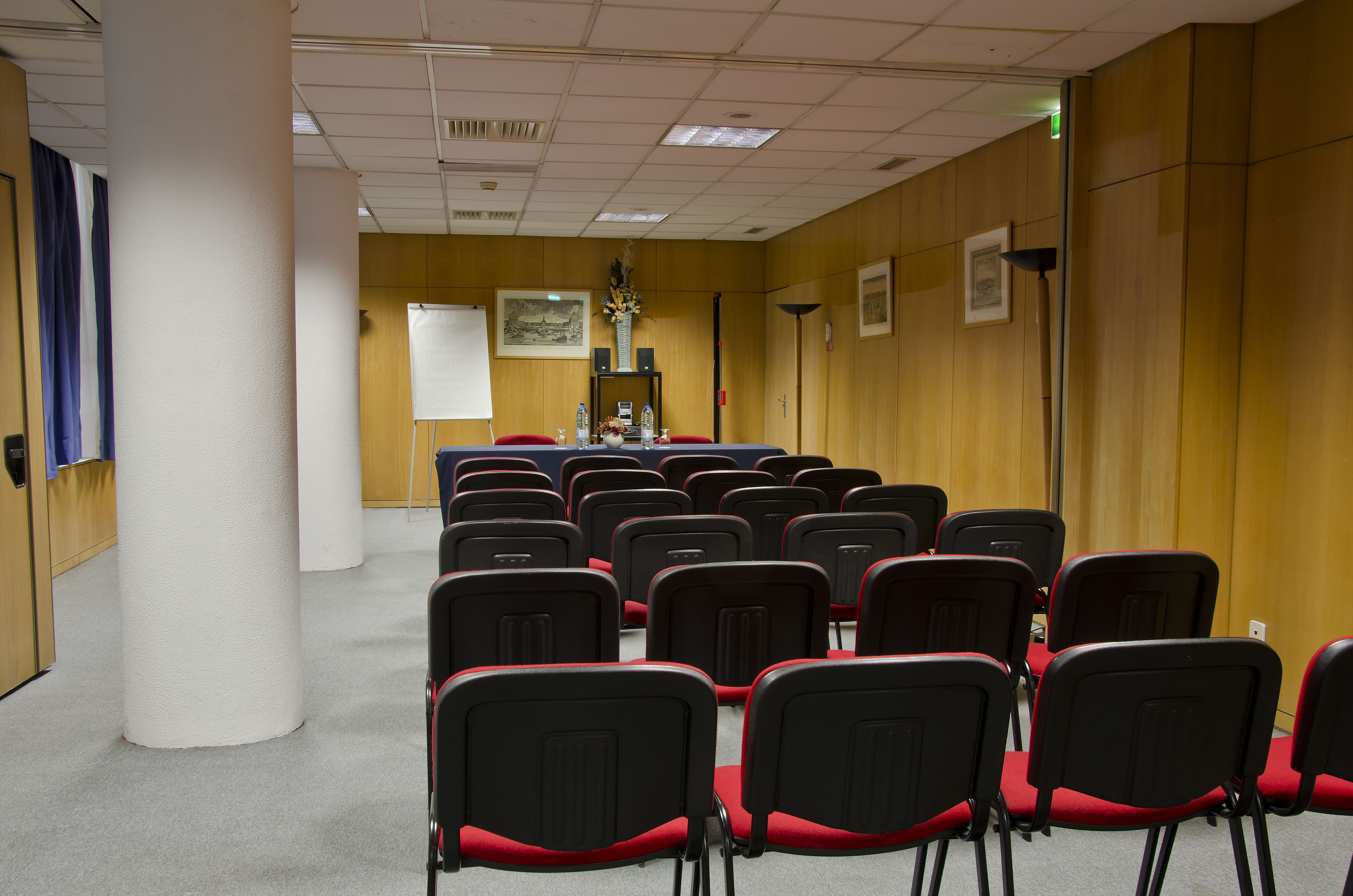 A conference room with rows of black chairs with red cushions, a whiteboard, and a projector screen.