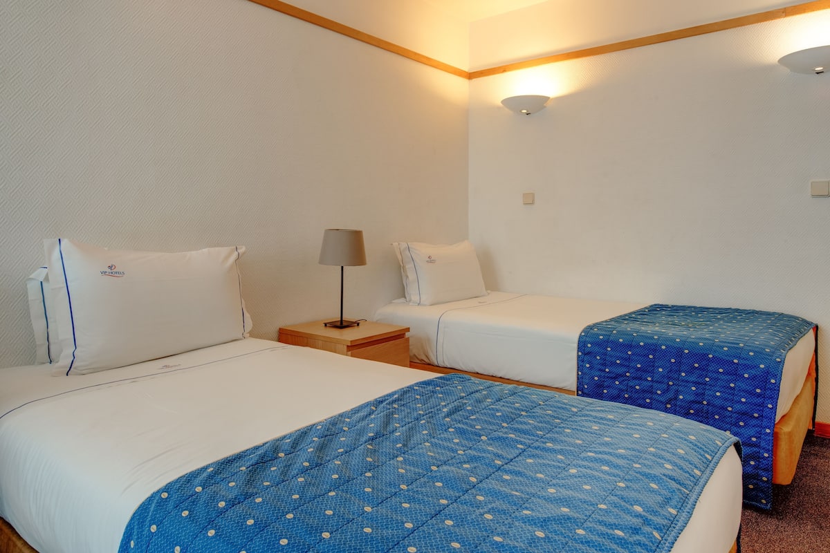 Ein Hotelzimmer mit zwei Betten, einem Nachttisch, einer Lampe und einer Wandleuchte.