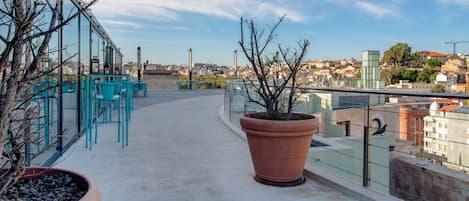 A rooftop terrace with outdoor seating, a large terracotta pot, and a view of the cityscape.