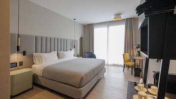 A hotel room with a bed, bedside tables, a desk with a chair, a television, and a window with curtains.