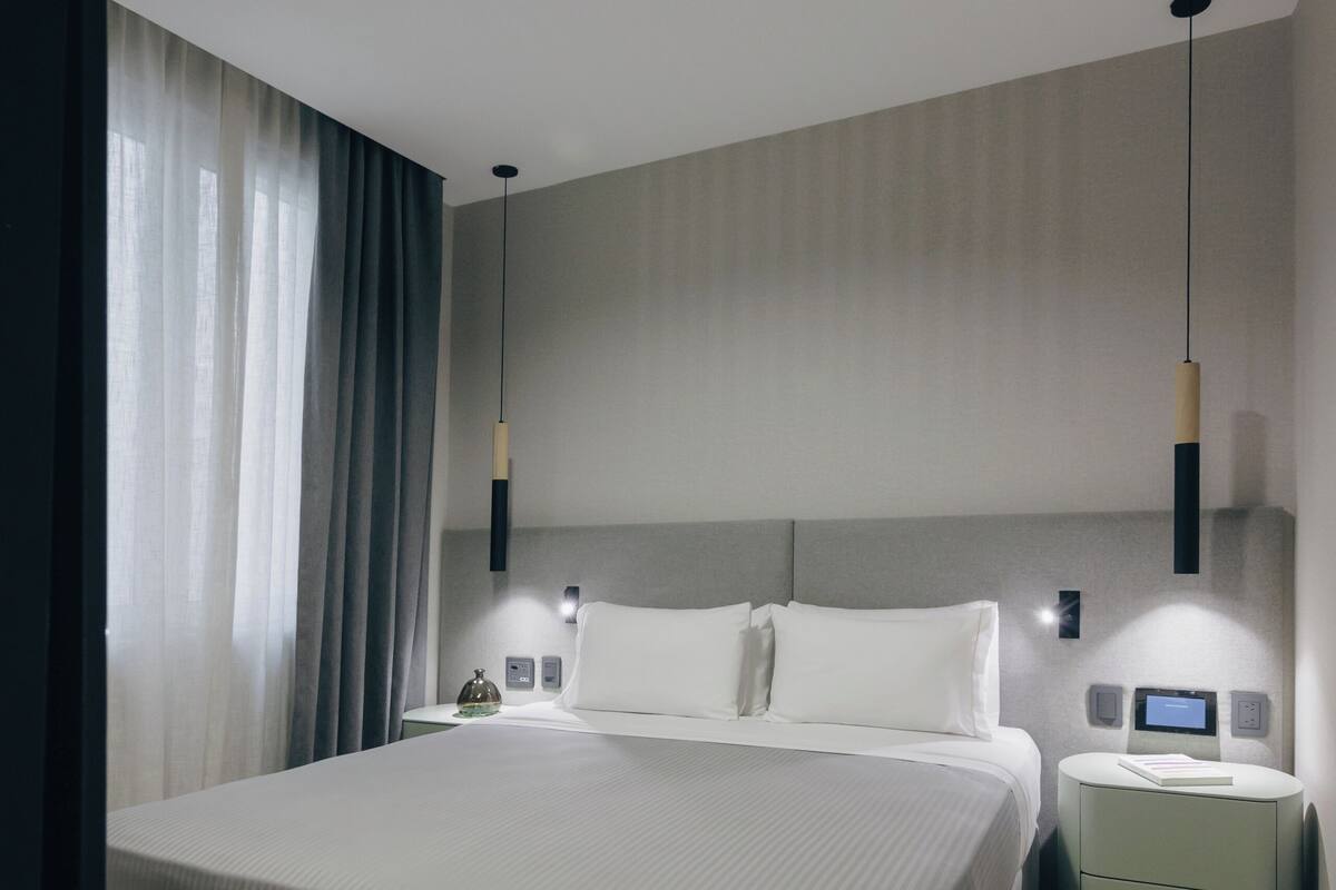 Una habitación de hotel moderna con una cama grande, mesitas de noche y una lámpara colgante.