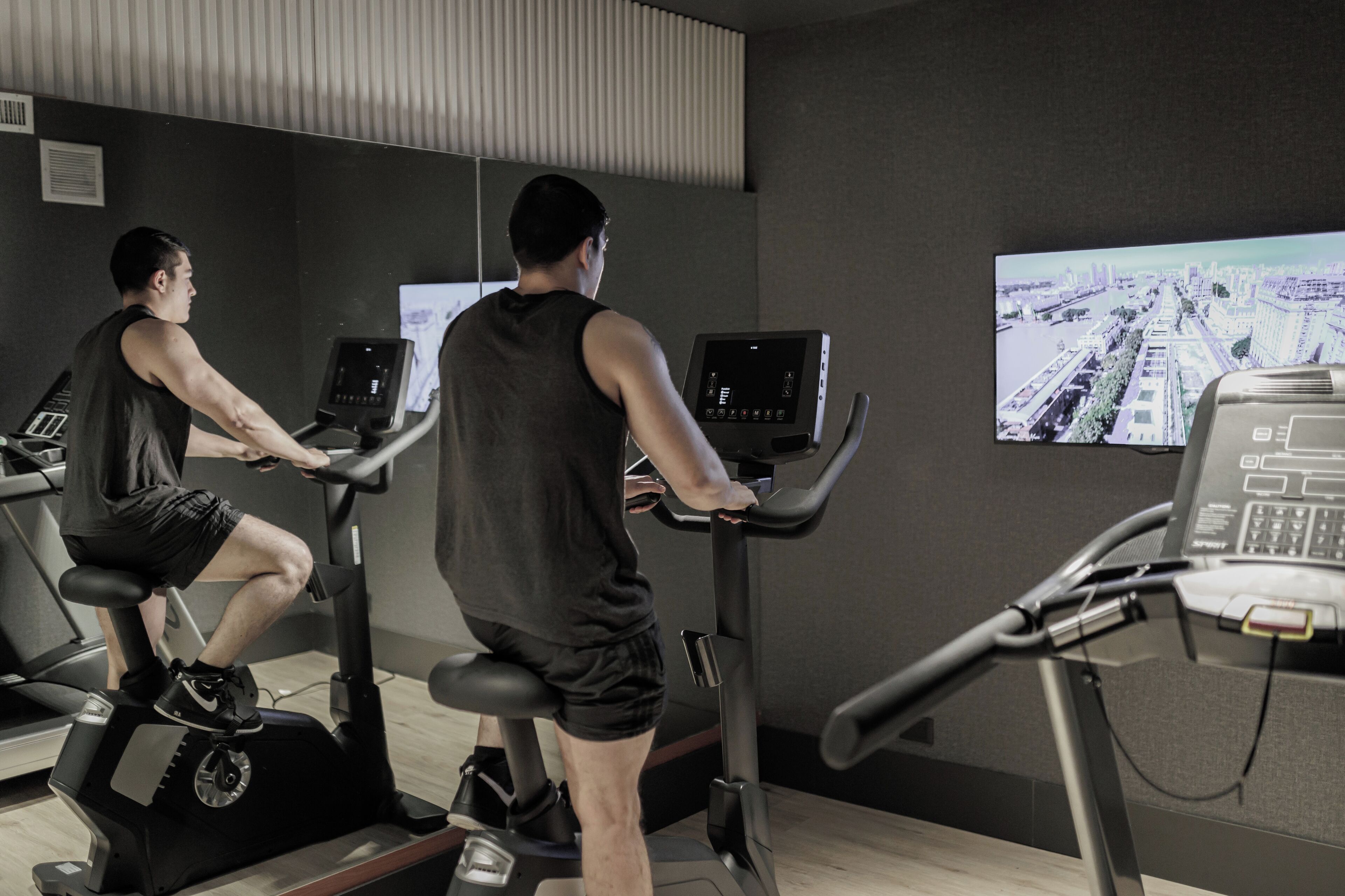 Two individuals using stationary bikes with digital screens in a gym.