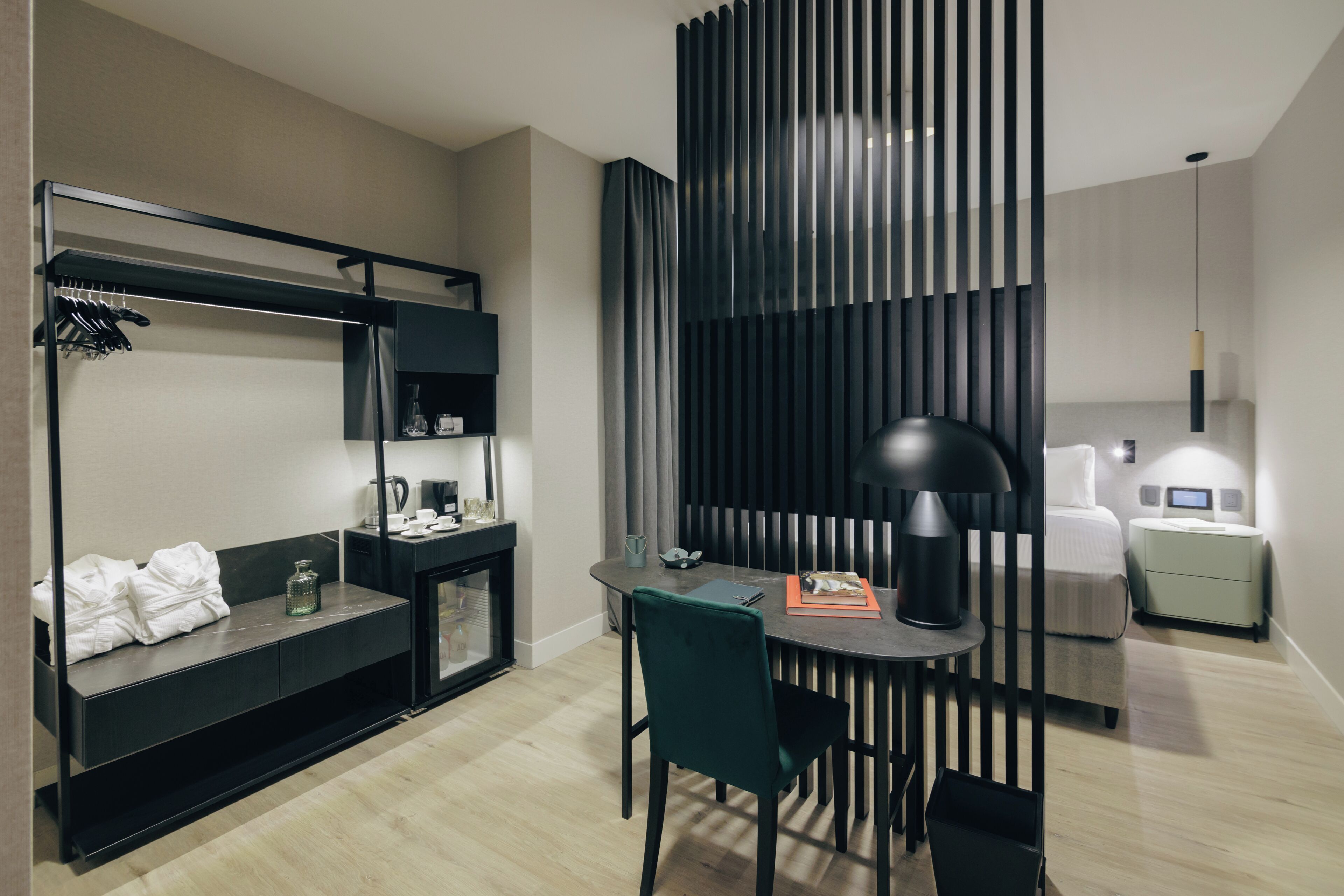 A modern hotel room with a bunk bed, a desk with a chair, a small table, a lamp, a bedside table with a lamp, and a nightstand.
