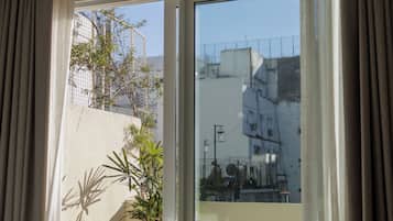 Habitación con puerta corrediza de vidrio que da a un balcón exterior con vistas a edificios y una valla.