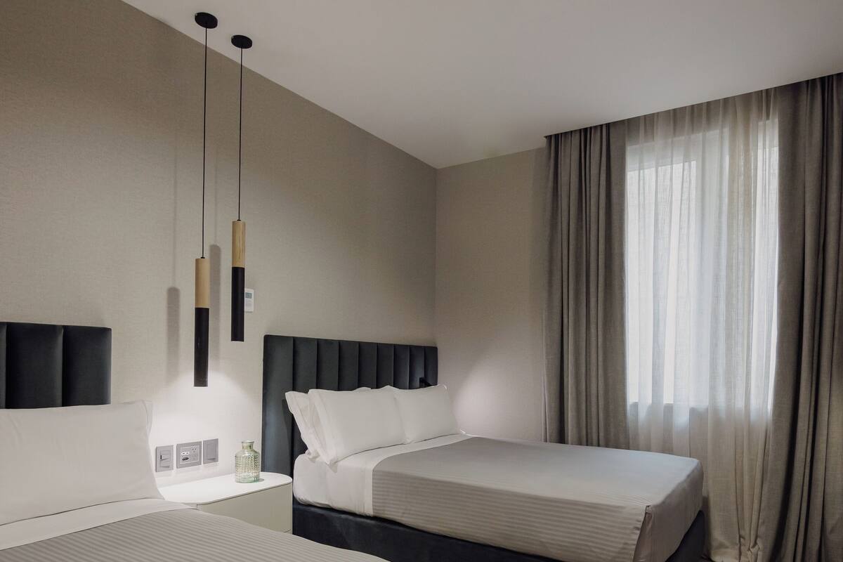 Una habitación de hotel moderna con dos camas, un ventanal con cortinas y una lámpara en el techo.