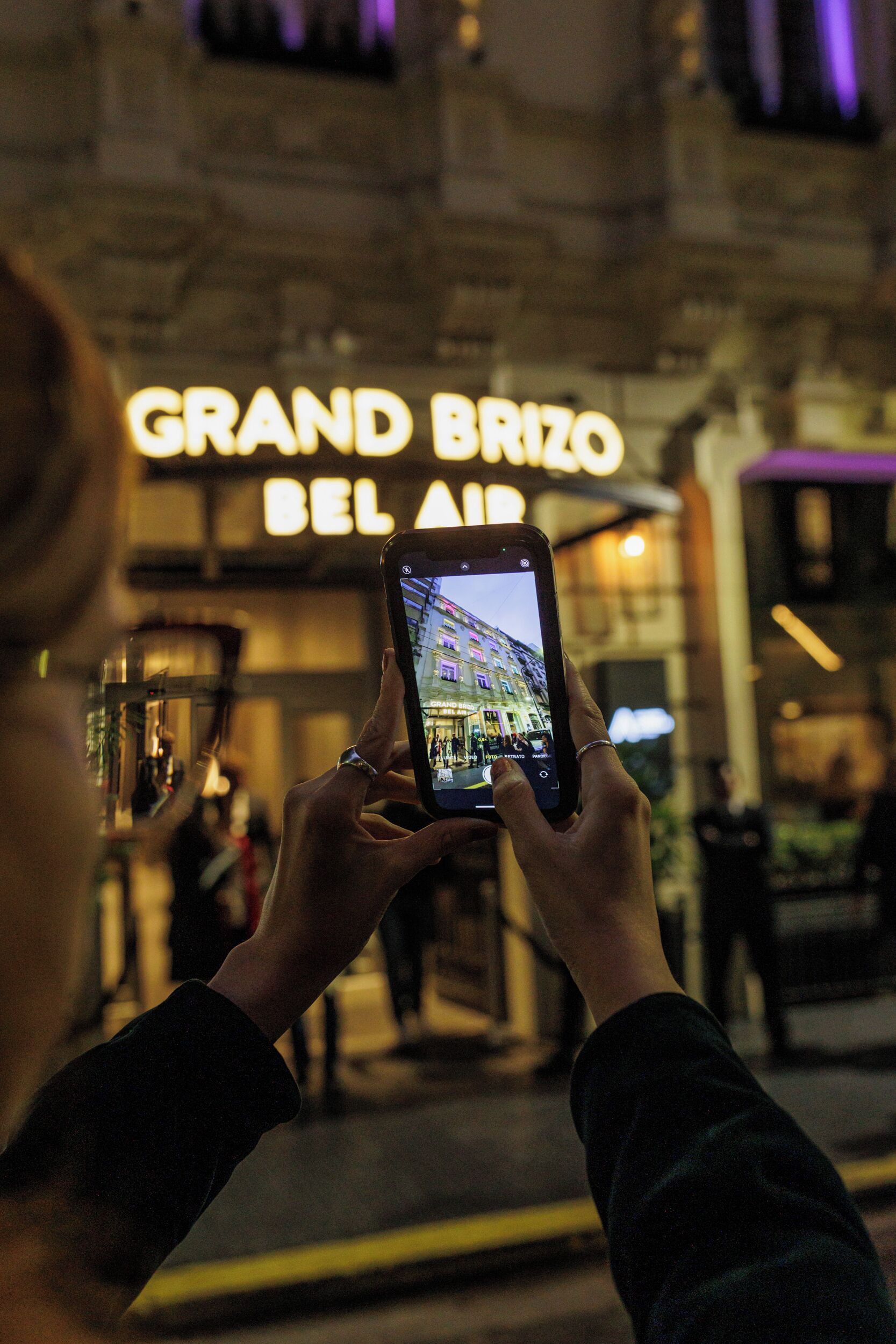 Una persona fotografiando un edificio con un cartel que dice 'GRAND BRIZO BEL AIR'.