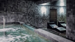 Un área de spa con pared de azulejos, bañera de hidromasaje y dos sillones de descanso.