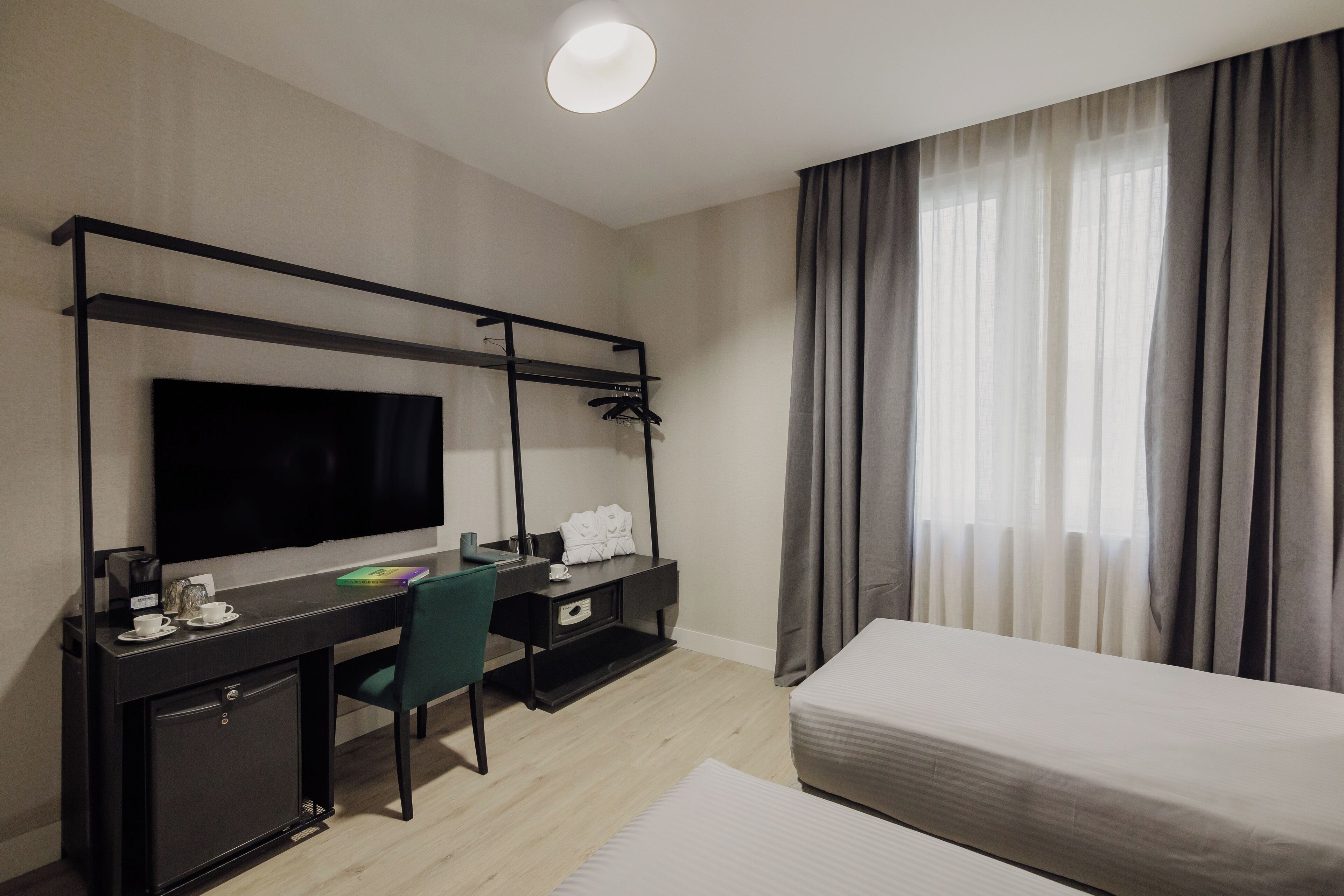 A hotel room with a bed, a desk with a TV, a chair, and a wardrobe.