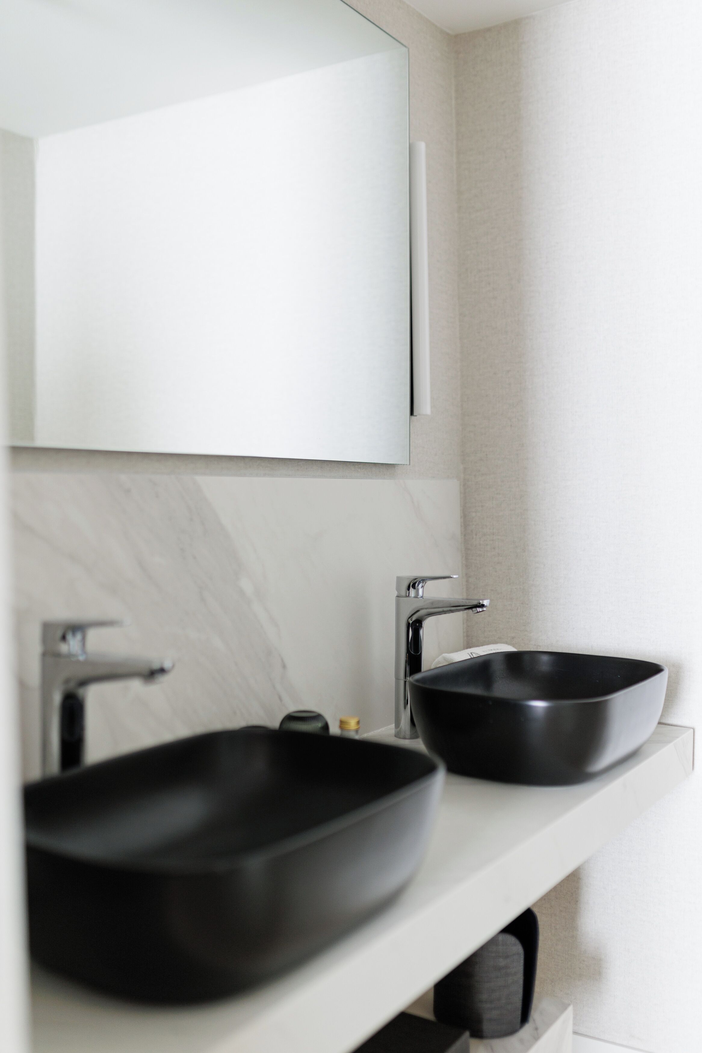 A bathroom with a white vanity, two black sinks, and a mirror.