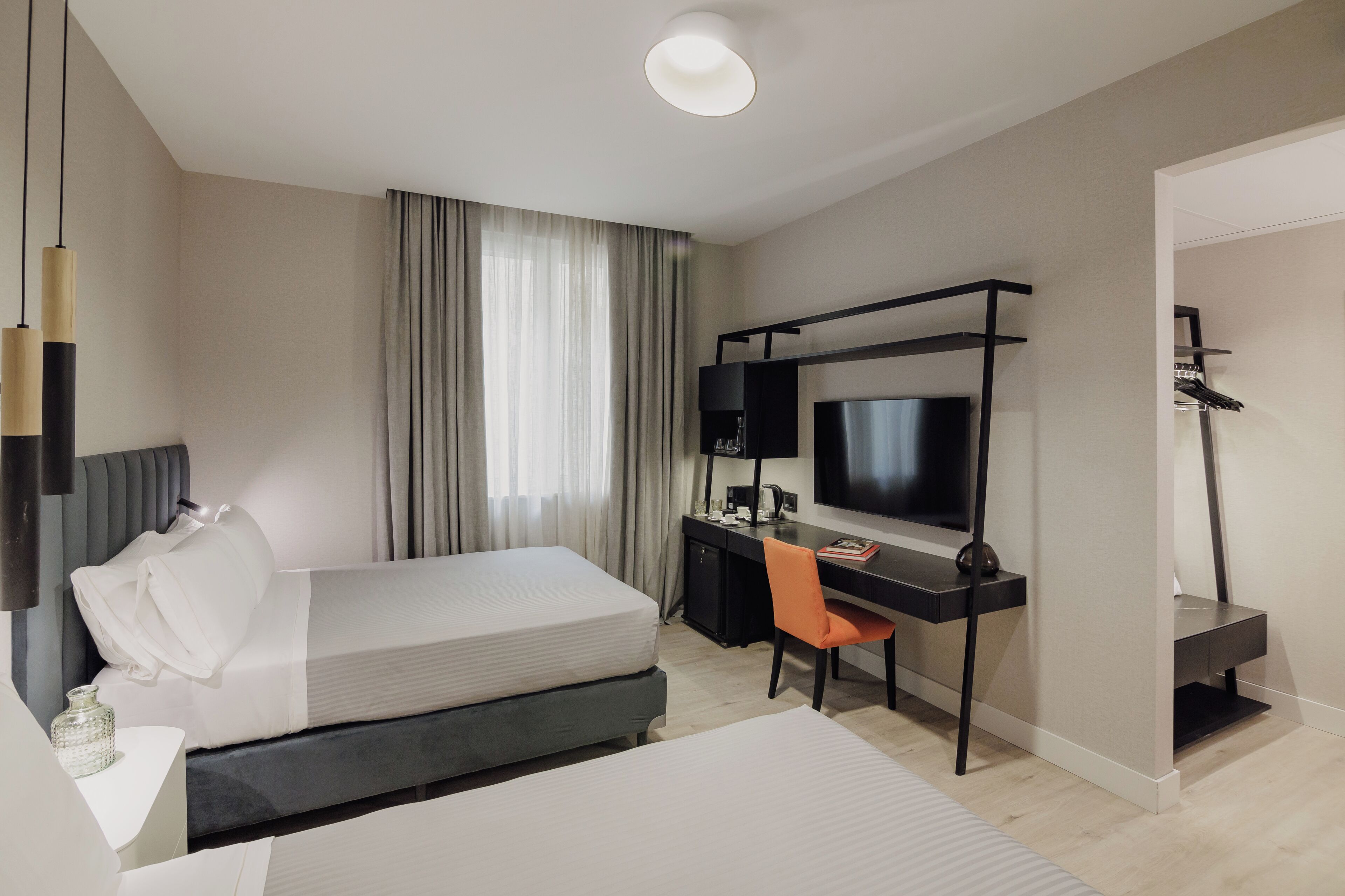 Habitació d'hotel moderna amb llit, escriptori, cadira, televisió i un armari encastrat.