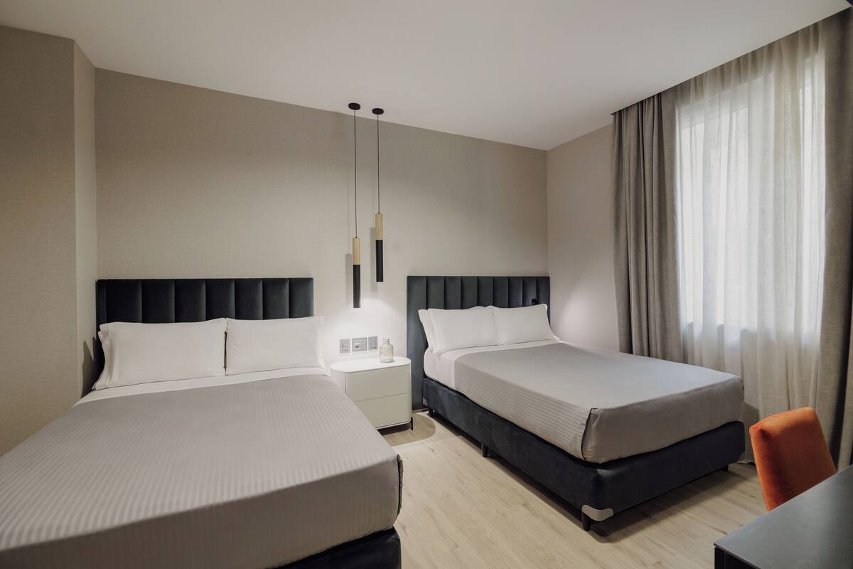 Habitación de hotel con dos camas, una mesita de noche, un escritorio y una silla.