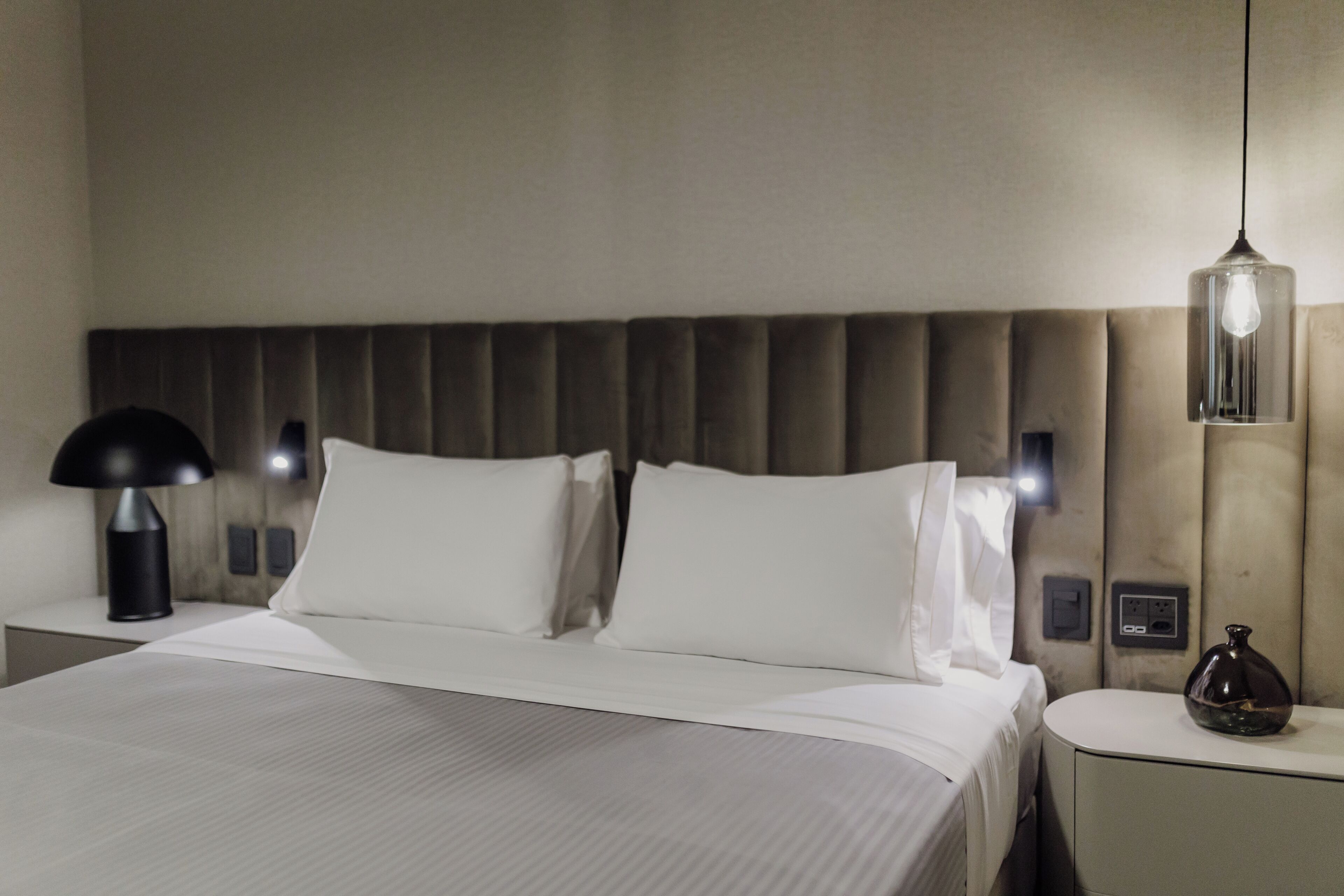 Habitació d'hotel amb un llit, taules de nit, una làmpada i una làmpada penjada a la paret.