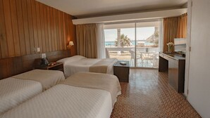 A hotel room with two beds, a desk, a chair, a TV, and a balcony with a view of the beach. - Hotel Arica (Arica)