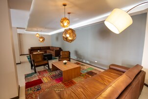 A modern living room with a leather sofa, a wooden coffee table, and a patterned rug. There are two hanging pendant lights and a floor lamp.