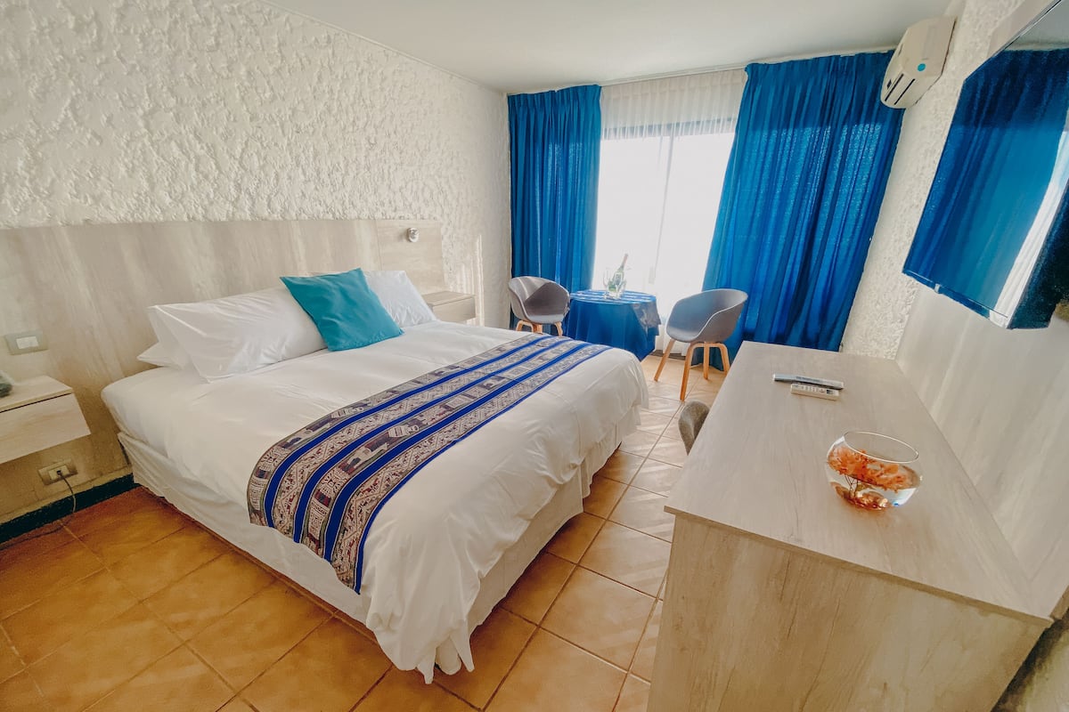 A hotel room with a bed, a desk, a chair, a small table, and a window with curtains.