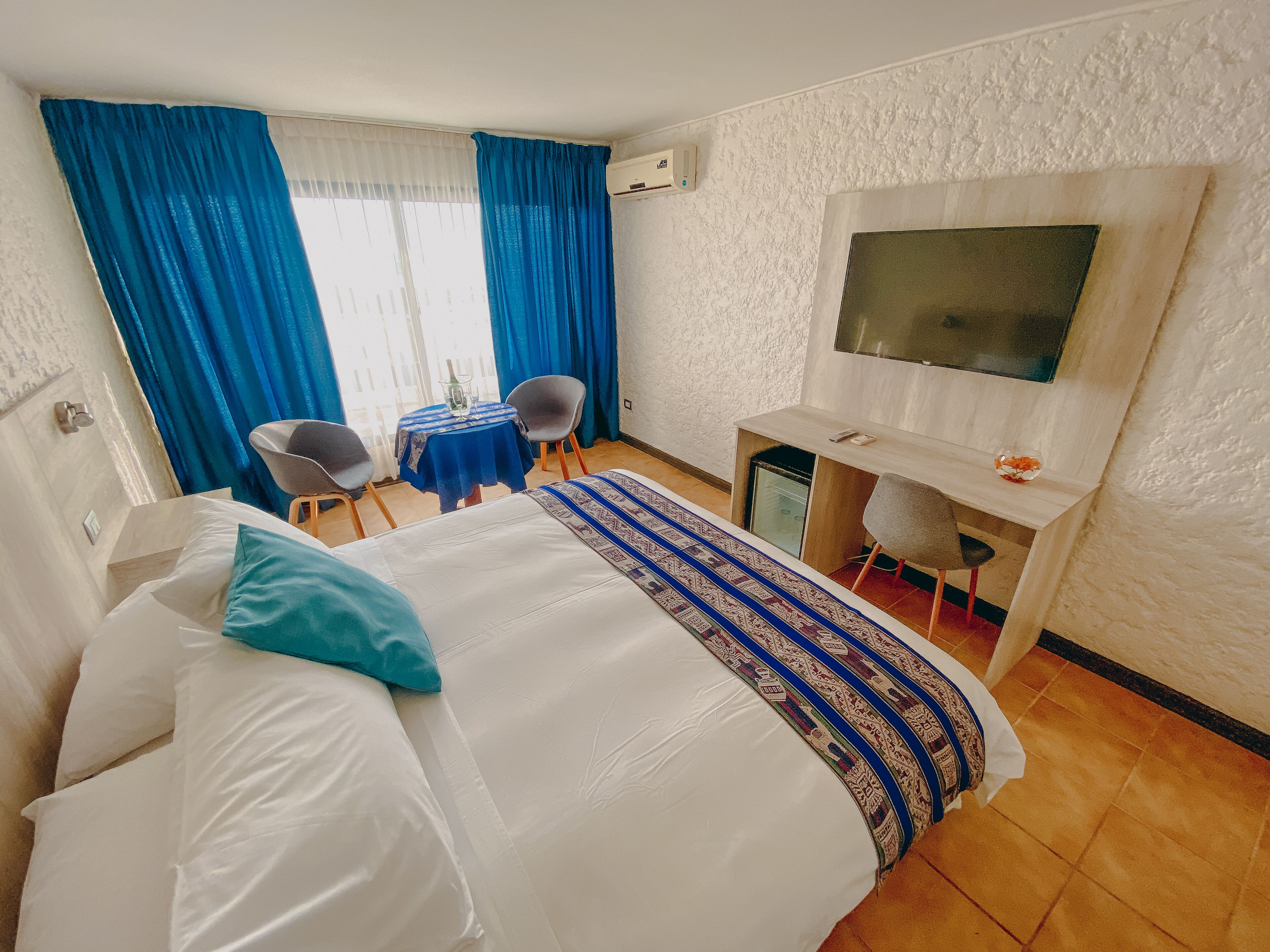 Habitación de hotel con cama, escritorio, silla, televisor y ventana con cortinas.