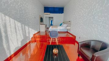 Hotellihuone, jossa on sänky, työpöytä, tuoli ja punamustaruudullinen laattalattia.