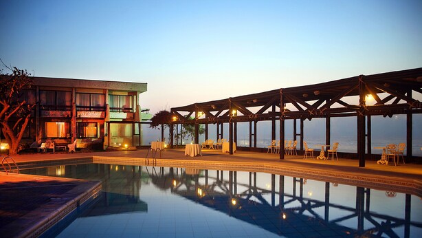 A poolside area with a covered seating area, a building with multiple balconies, and a view of the water. - Hotel Arica (Arica)