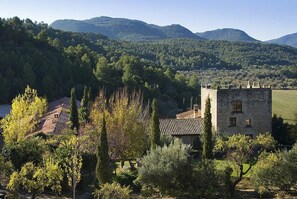 A stone tower with a tiled roof, surrounded by trees and hills in the background. - La Torre del Visco (Fuentespalda)