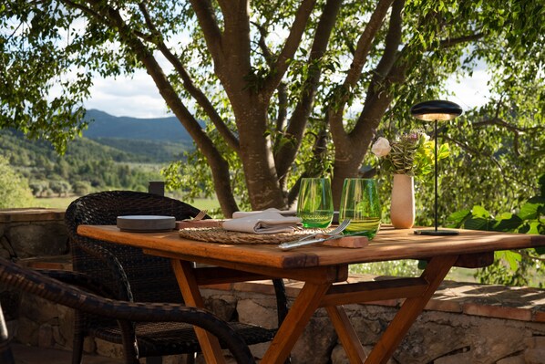 Un espace de restauration en plein air avec une table en bois, des chaises en osier et une vue sur un paysage montagneux.