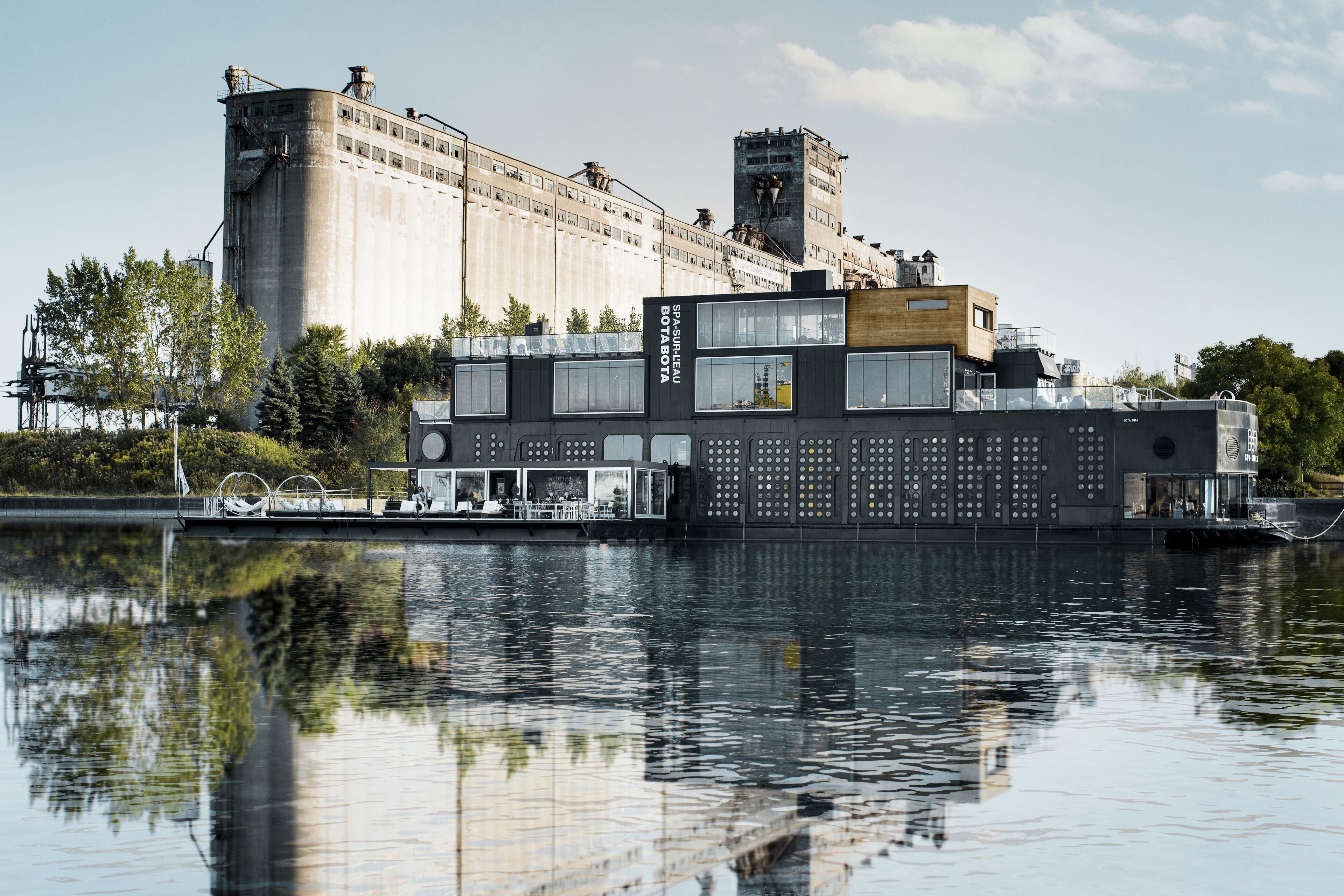 Ein modernes Gebäude mit flachem Dach und großen Fenstern, gelegen an einem ruhigen Gewässer.