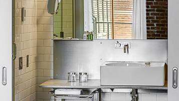 A modern bathroom with a white tiled wall, a large mirror, a sink, and a window with blinds.