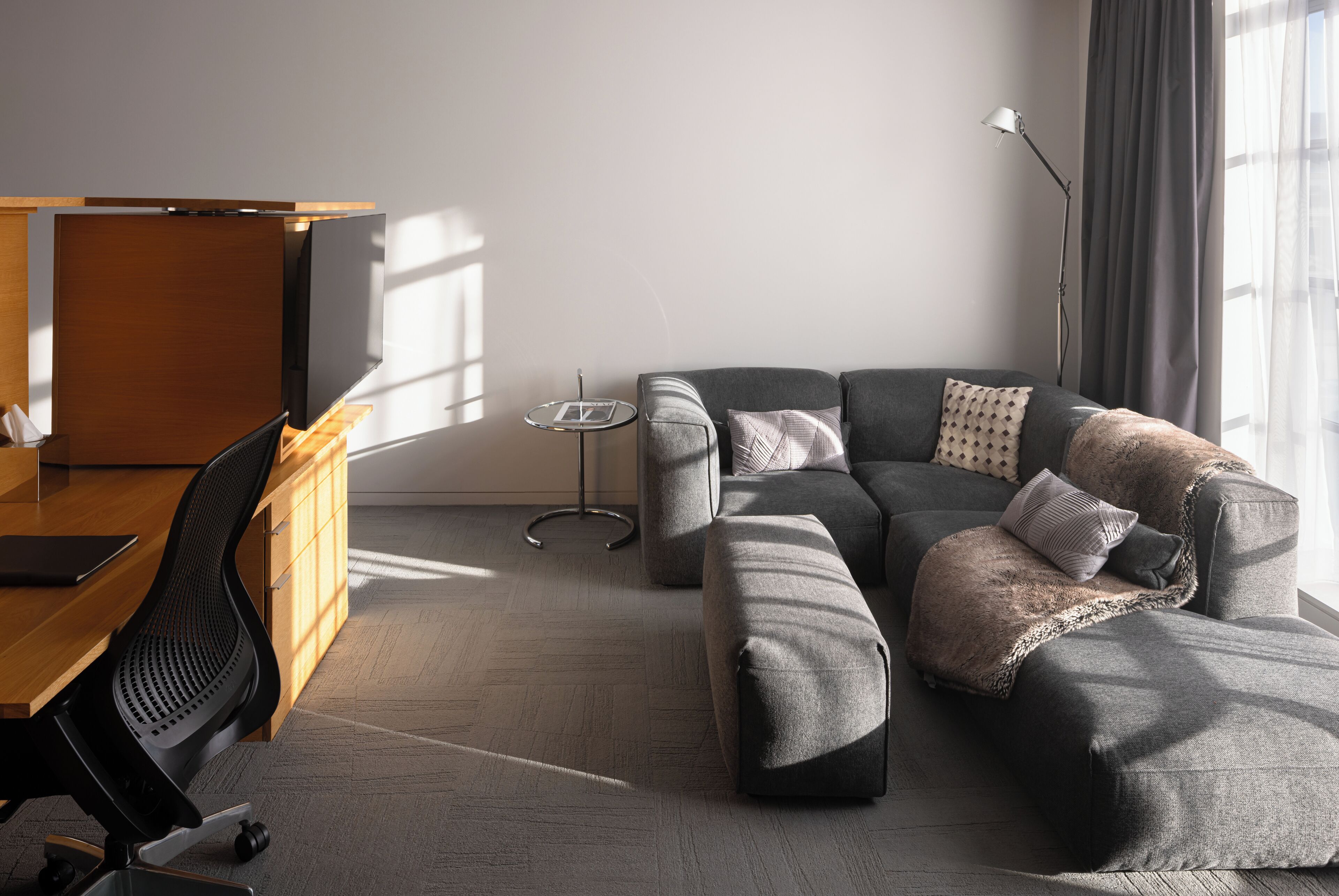 A modern living room with a sofa, ottoman, and a desk with a chair.