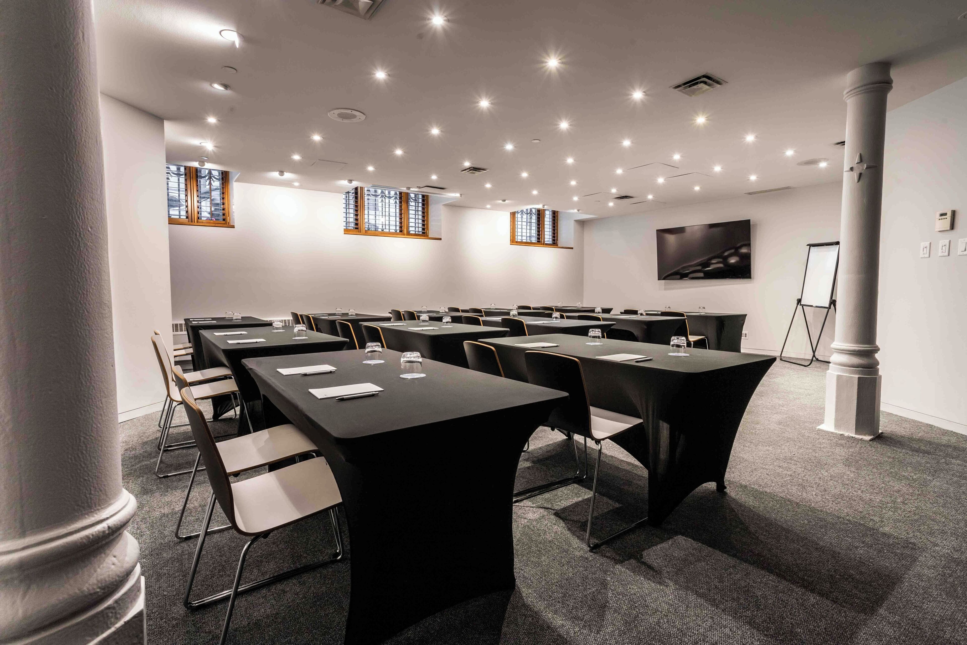 Una sala conferenze con diversi tavoli e sedie, uno schermo per proiettore e un'ampia finestra vista alberi.