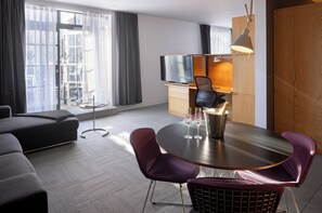 A modern hotel room with a sofa, a dining table with chairs, a TV, and a minibar. - Hotel Gault (Montreal)
