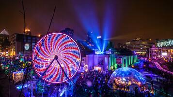A large Ferris wheel and a dome-shaped structure in a cityscape at night.