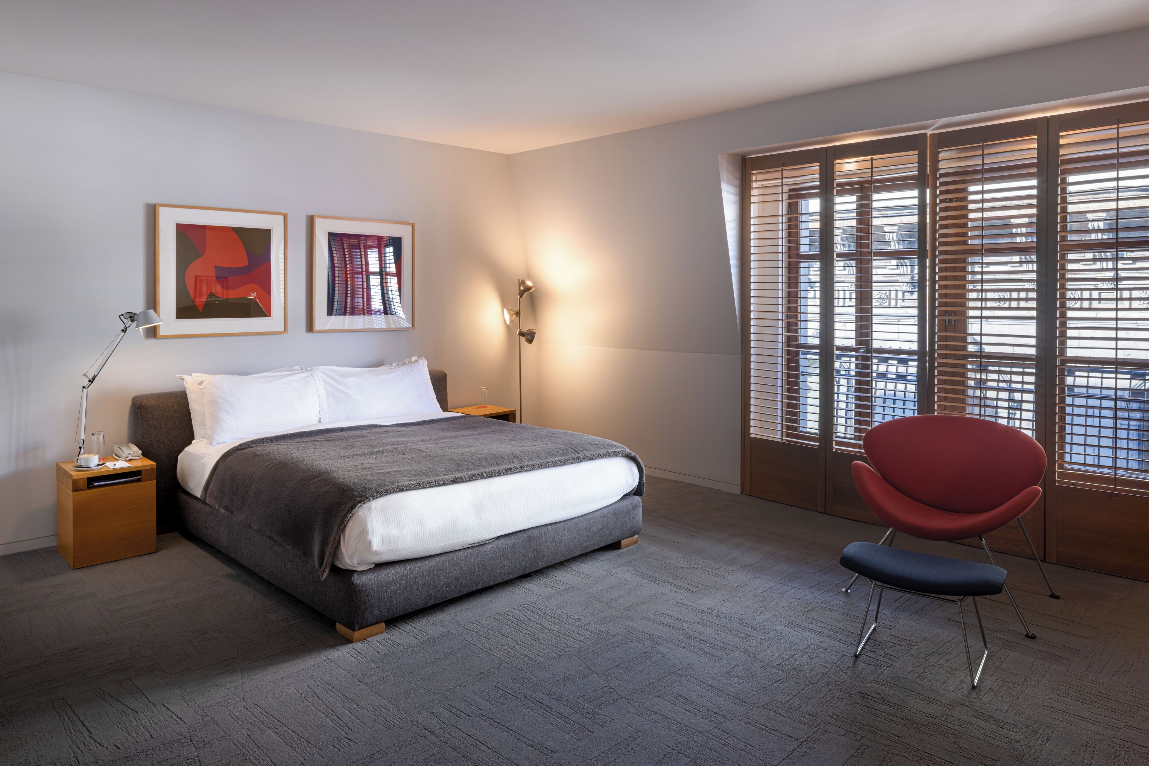 Ein modernes Schlafzimmer mit einem großen Bett, Nachttischen, einem roten Sessel und einem Fenster mit Jalousien.