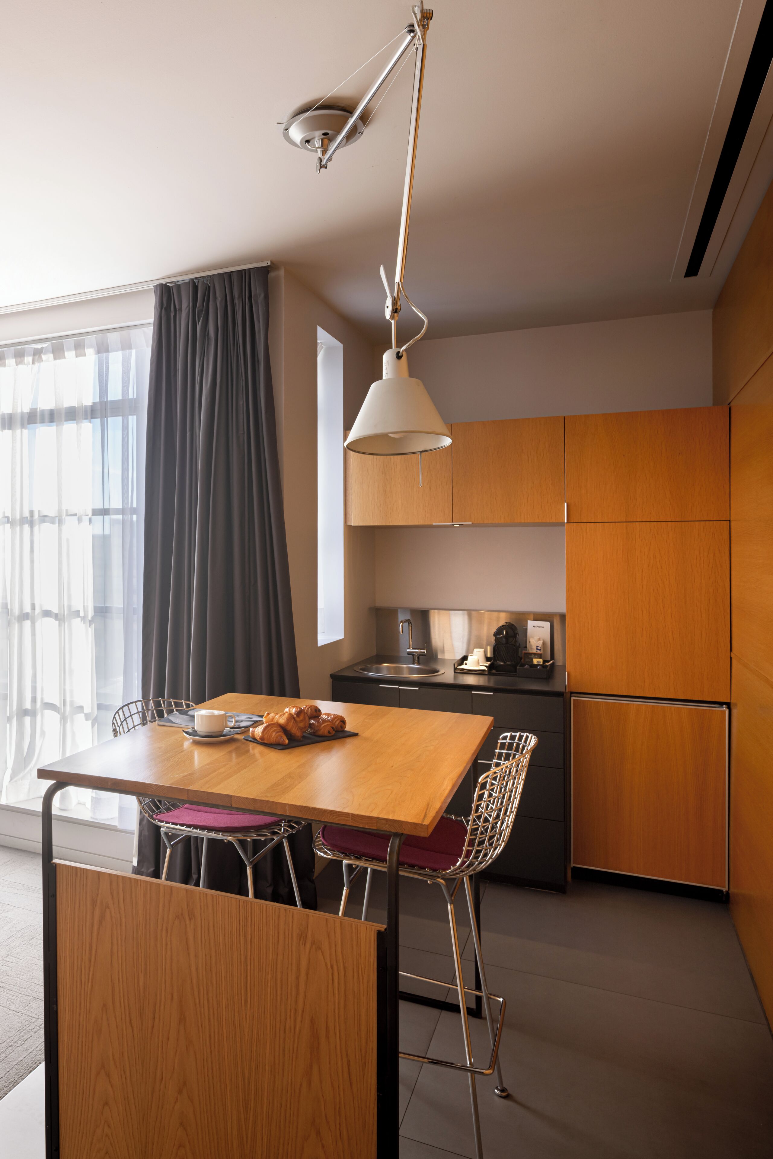 Una cocina moderna con una mesa de madera, taburetes de bar, una cafetera y un refrigerador.