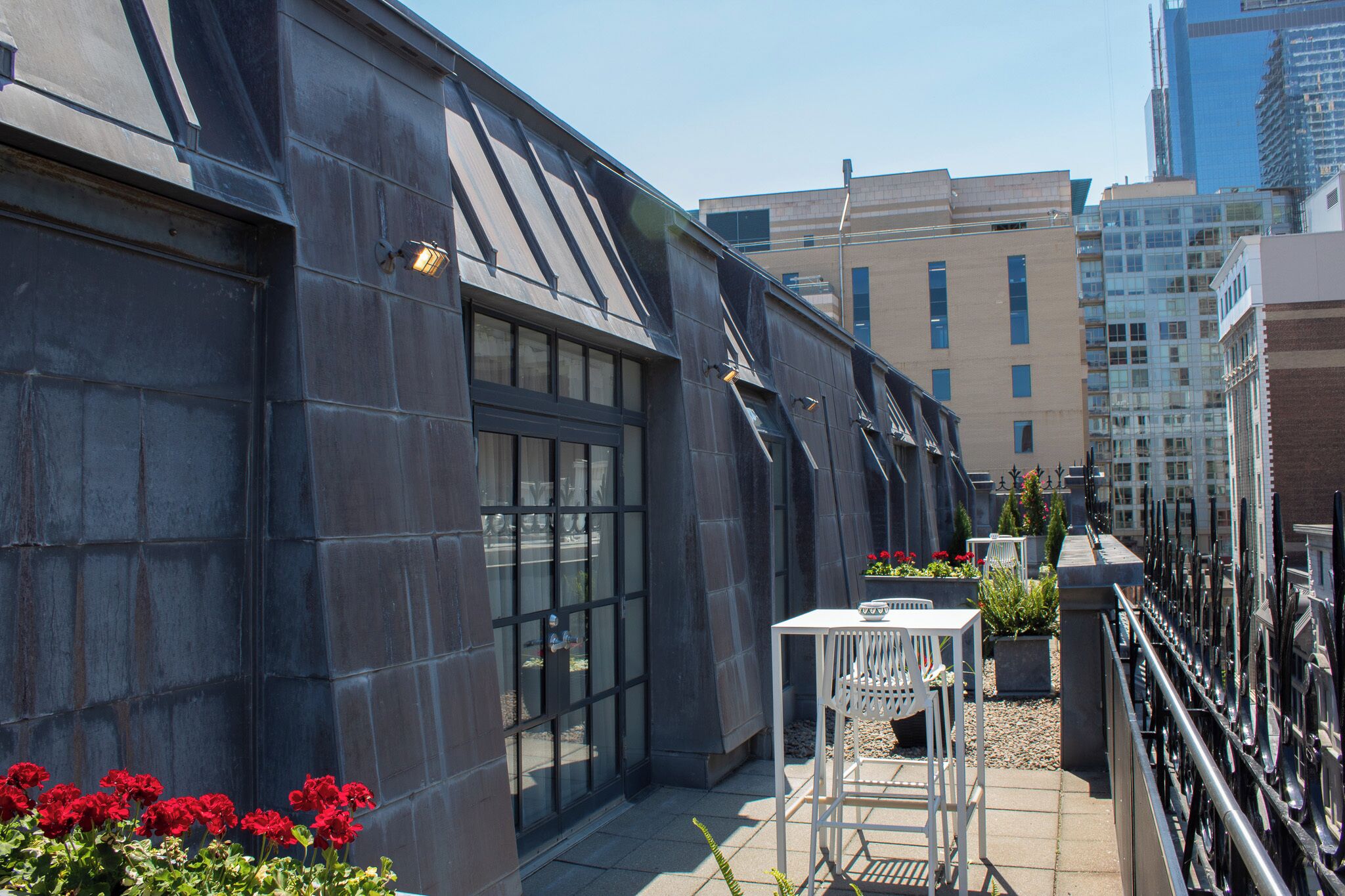 A rooftop terrace with a modern building, a table with chairs, and potted plants.