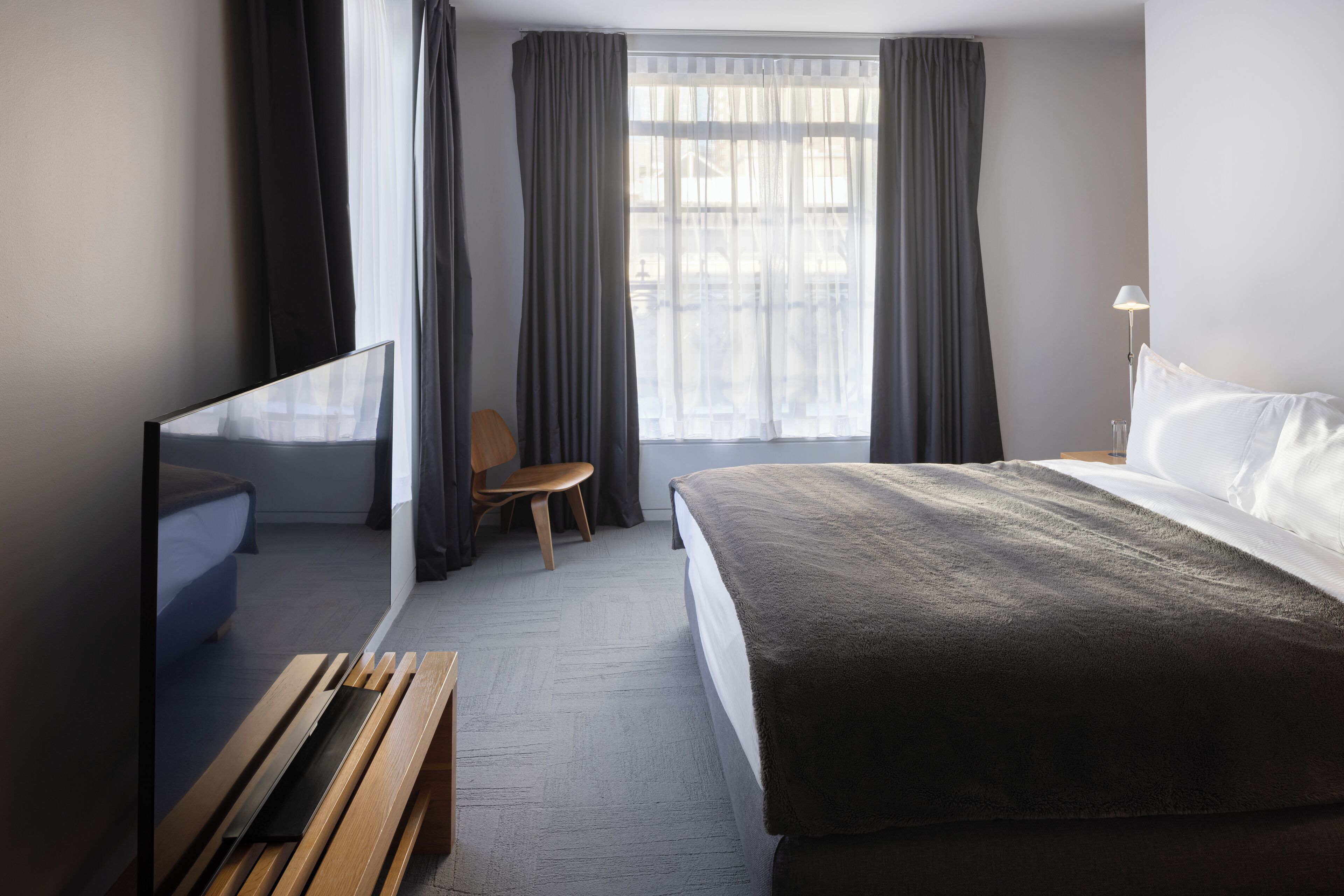 A hotel room with a bed, a TV, a chair, and a desk.
