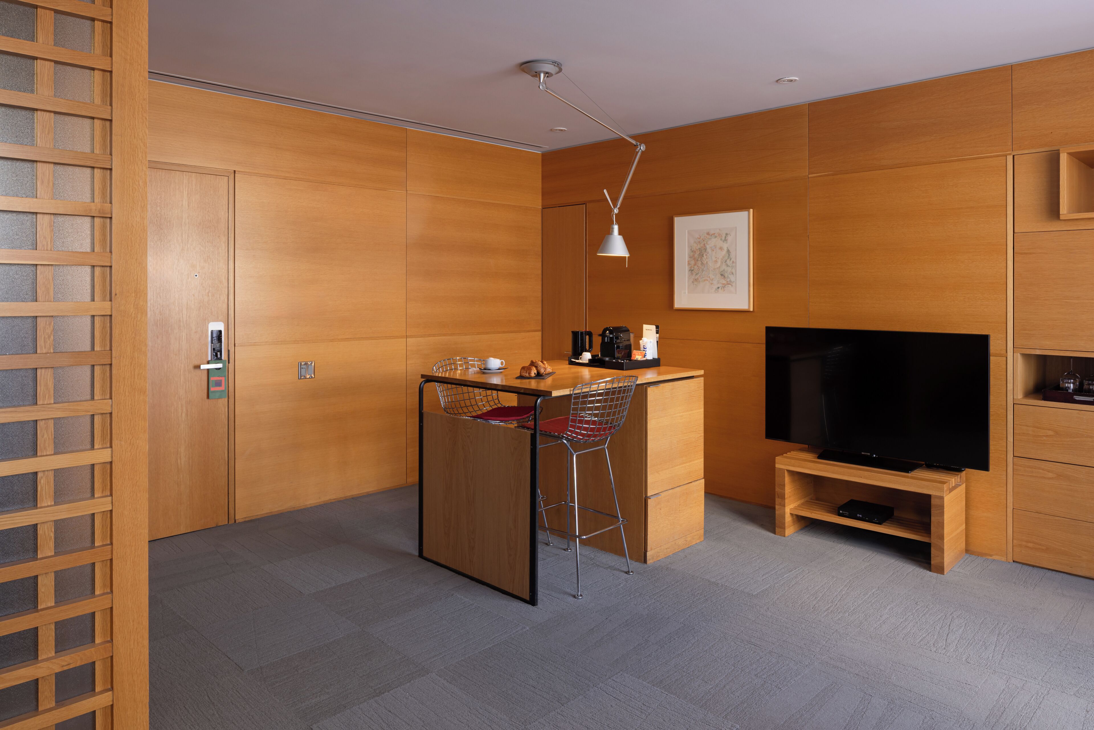 A modern kitchen with wooden cabinetry, a small island with bar stools, a coffee maker, and a flat-screen TV on a wooden stand.