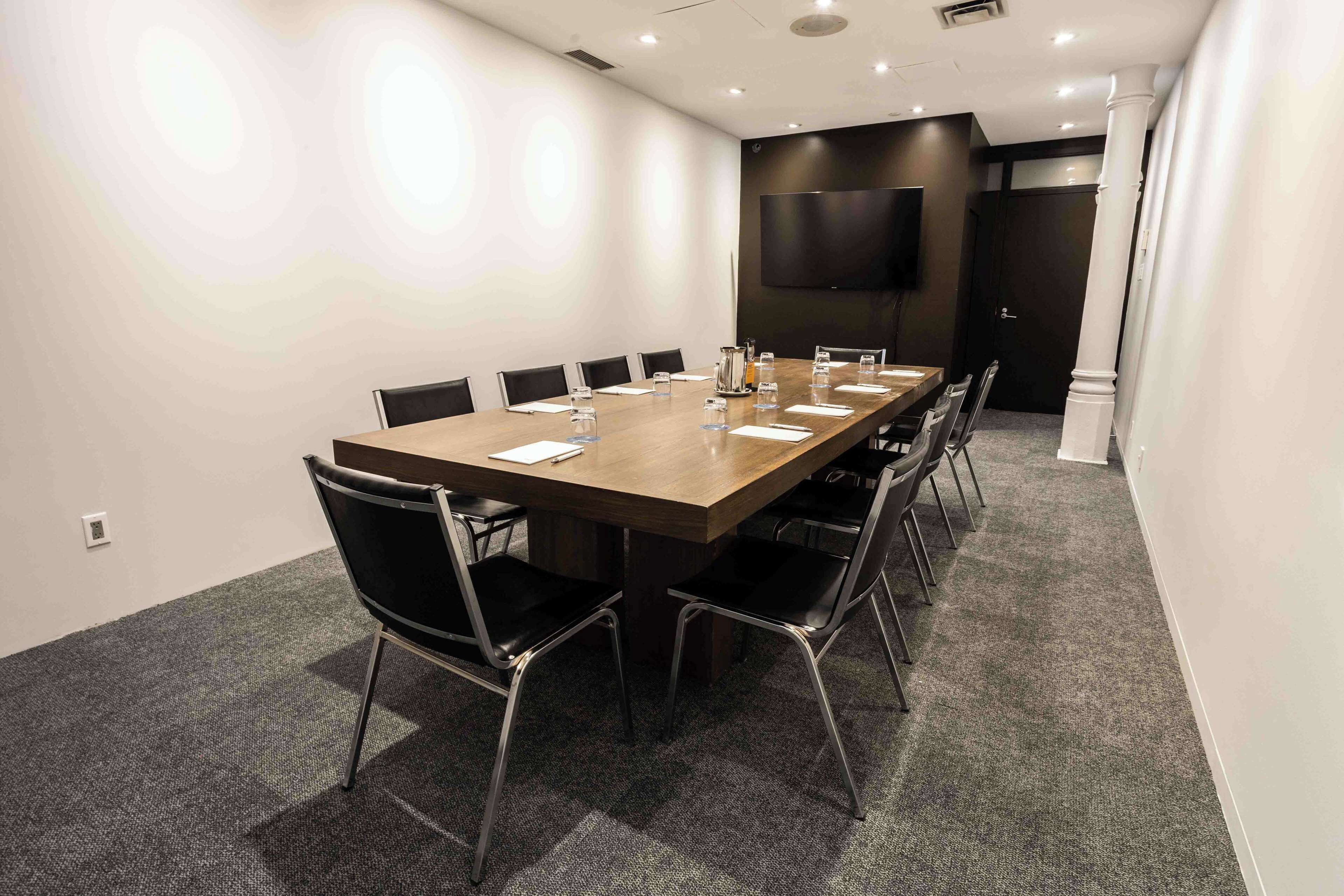 A conference room with a long table, black chairs, and a flat-screen TV on the wall.