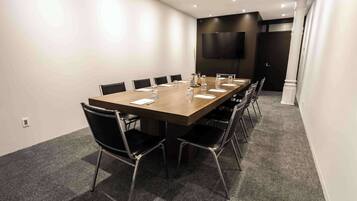 A conference room with a long table, black chairs, and a flat-screen TV on the wall.