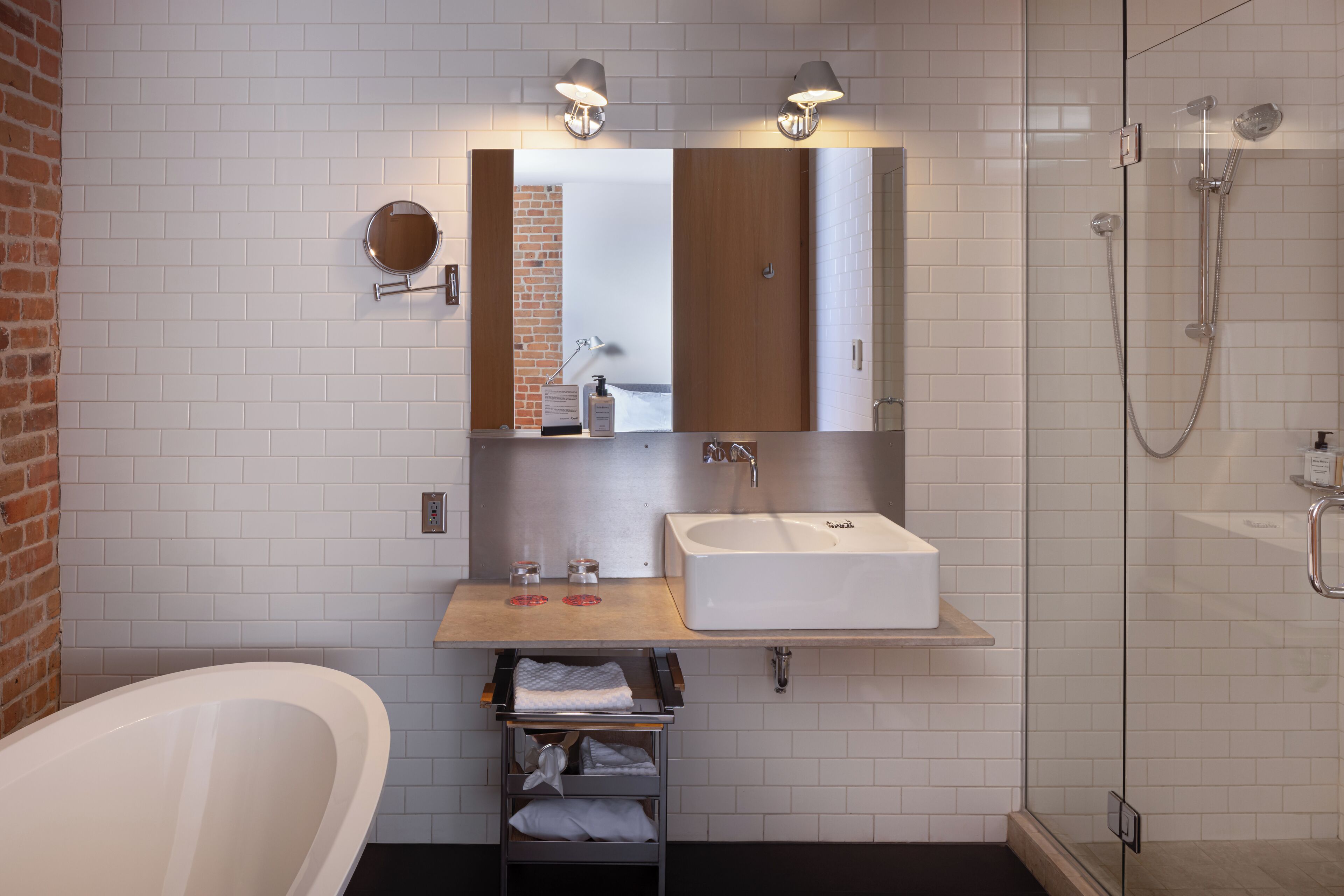 A modern bathroom with a freestanding bathtub, a large mirror, a sink with a wooden countertop, and a glass-enclosed shower area.