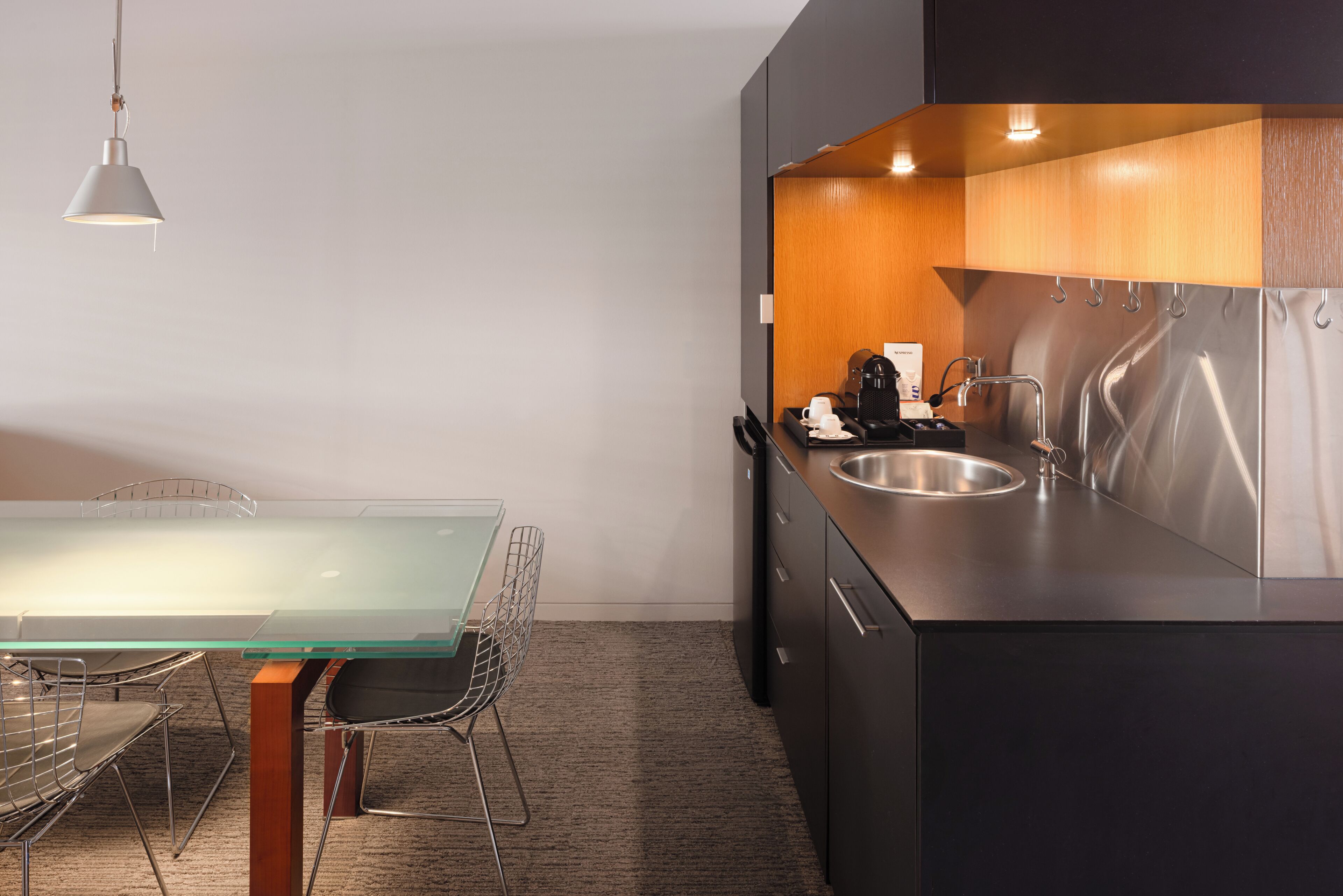 A modern kitchen with a stainless steel sink, a glass-top table, and a metal chair.