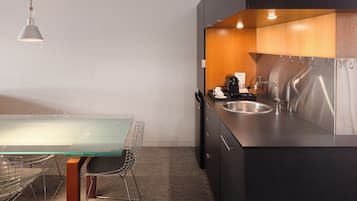 A modern kitchen with a stainless steel sink, a glass-top table, and a metal chair.