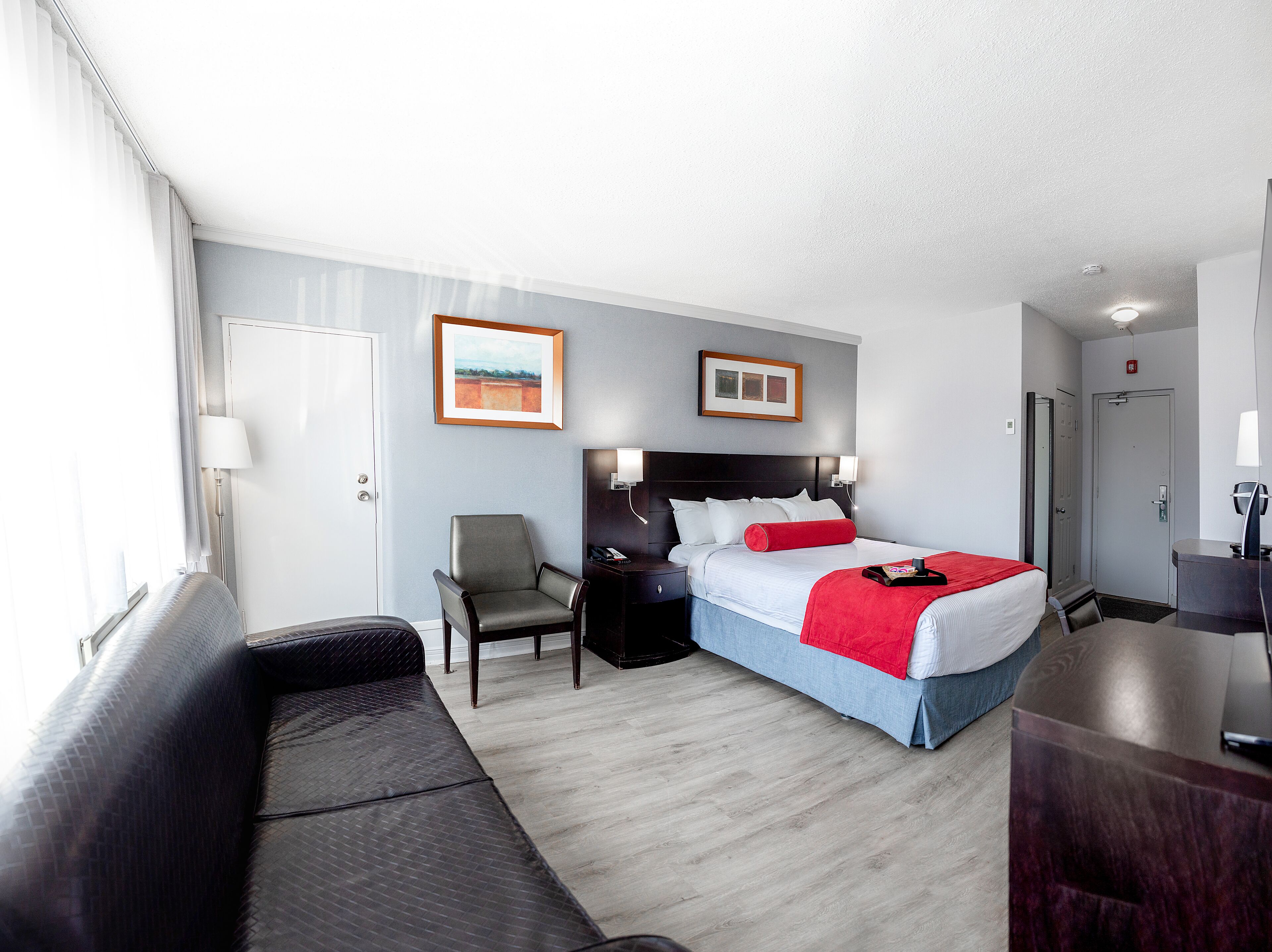 A hotel room with a bed, a chair, a desk, and a window.