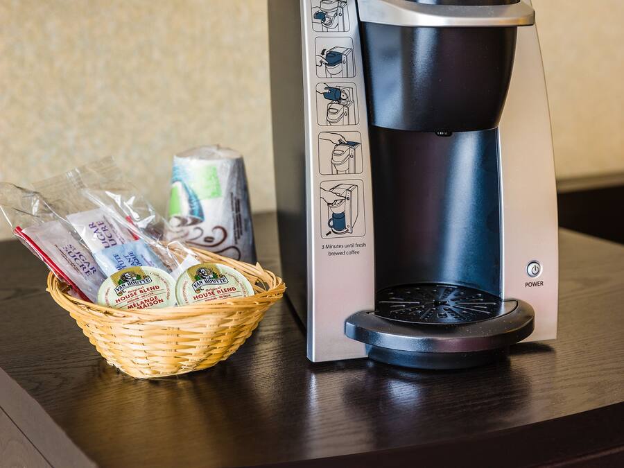 Una cafetera Keurig sobre una taula de fusta amb un cistell de càpsules de cafè i una llauna de refresc.