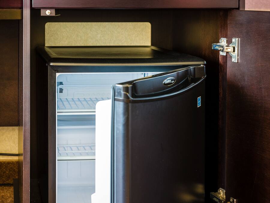 A compact refrigerator built into a wooden cabinet with a handle for opening.