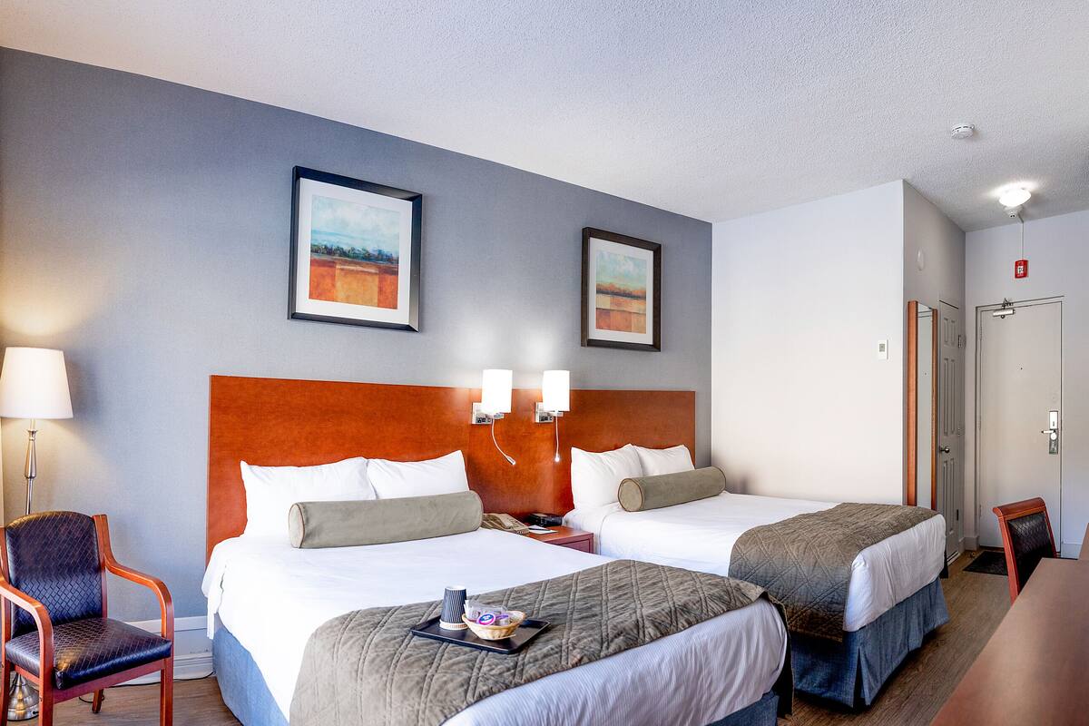 A hotel room with two beds, a chair, a desk, and a window with curtains.