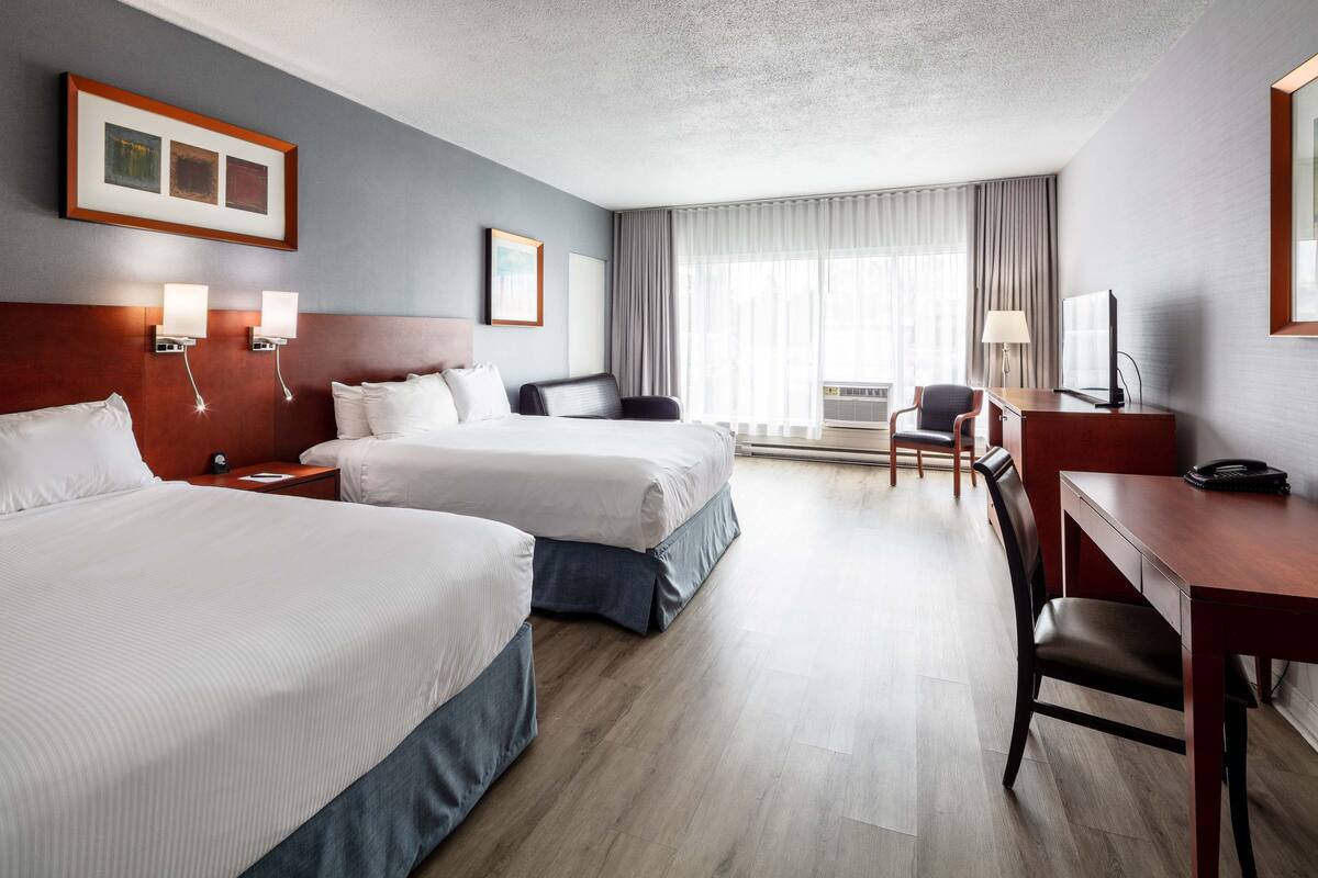 A hotel room with two beds, a desk, a chair, a TV, and a window with curtains.