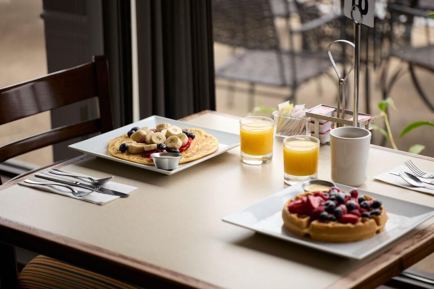 Ein Frühstückstisch mit Pfannkuchen, belegt mit Bananen und Beeren, ein Waffel mit Beeren und zwei Gläser Orangensaft.