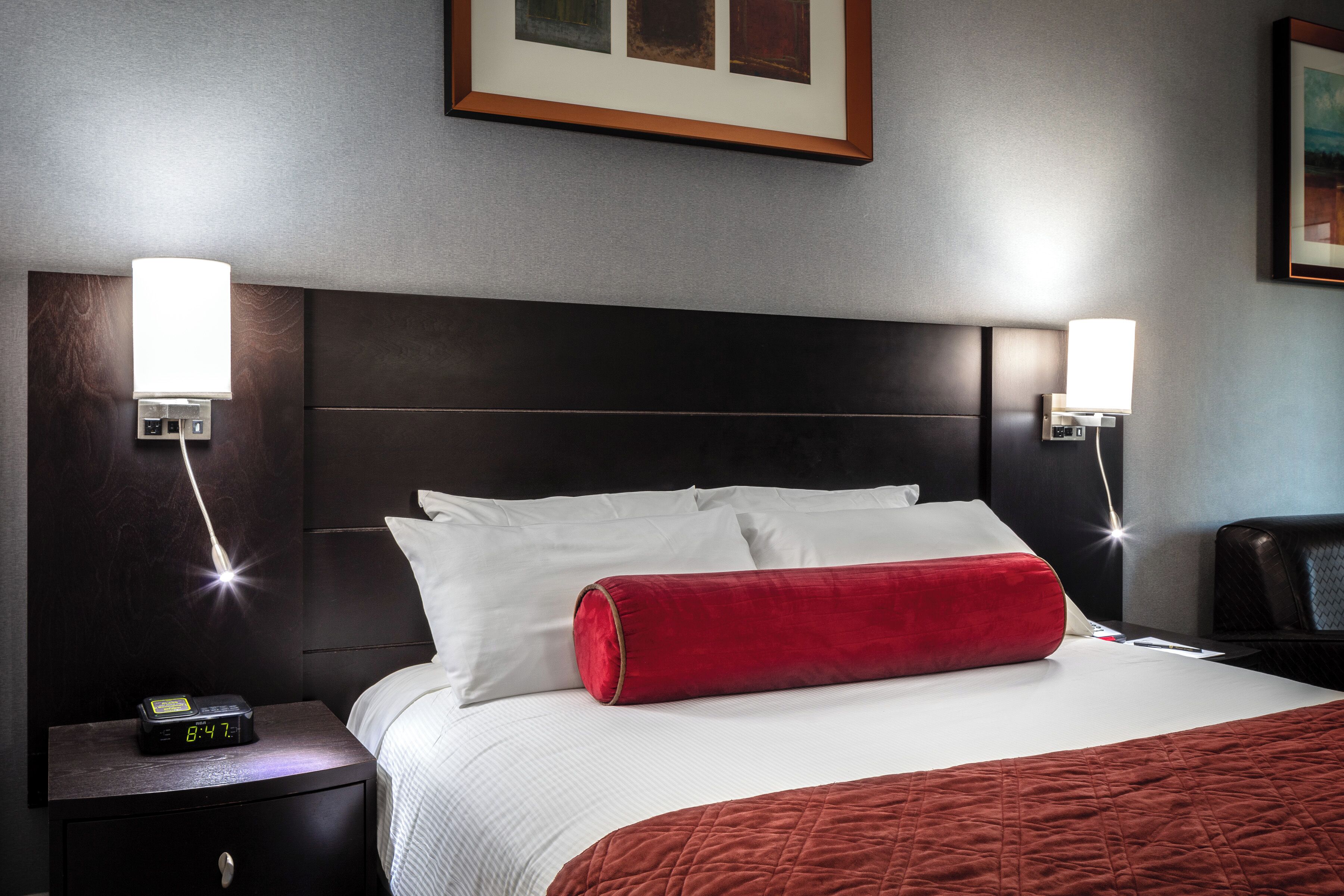 A hotel room with a bed, two bedside tables, a nightstand, and two wall-mounted lamps.