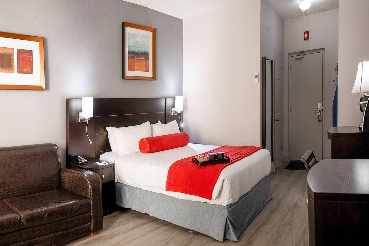 A hotel room with a bed, a leather sofa, a nightstand, and two framed pictures on the wall.