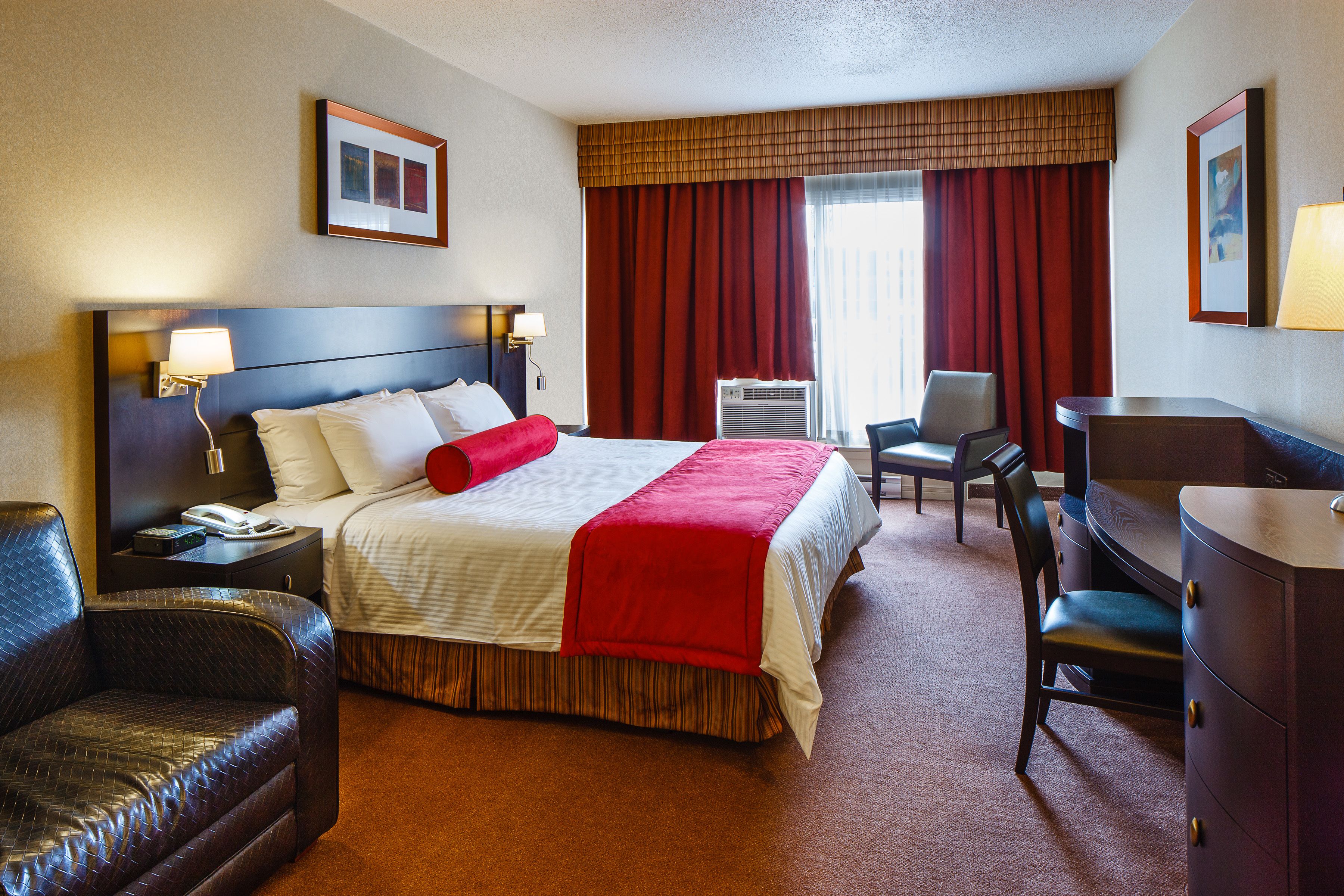 A hotel room with a large bed, a desk, a chair, a sofa, and an air conditioning unit.